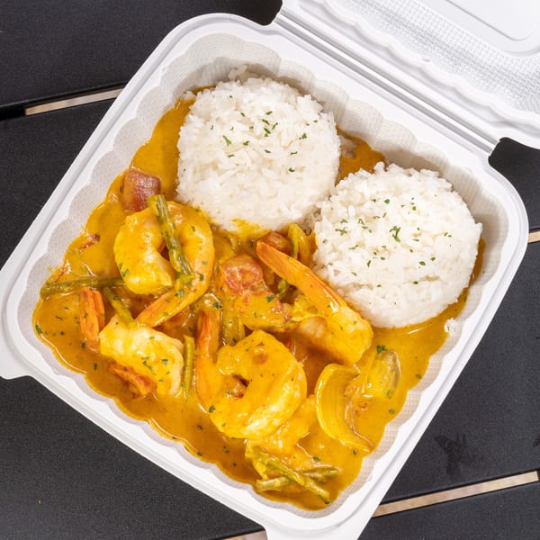 Shrimp curry with green beans and rice in a white takeout container on a dark table.