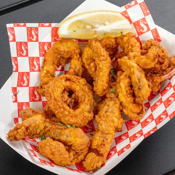 Crispy fried seafood, including shrimp and calamari, with a lemon wedge in a paper tray.