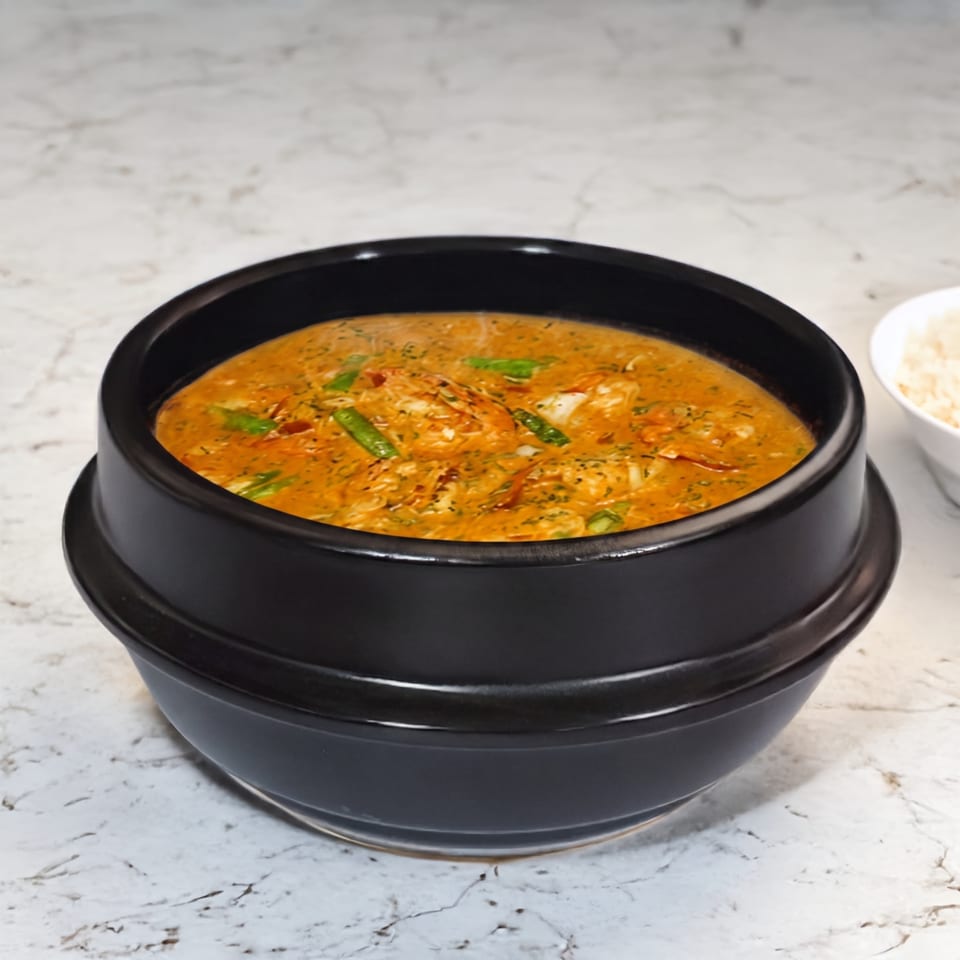 A black bowl of orange curry with green beans and shrimp, with a side of white rice.