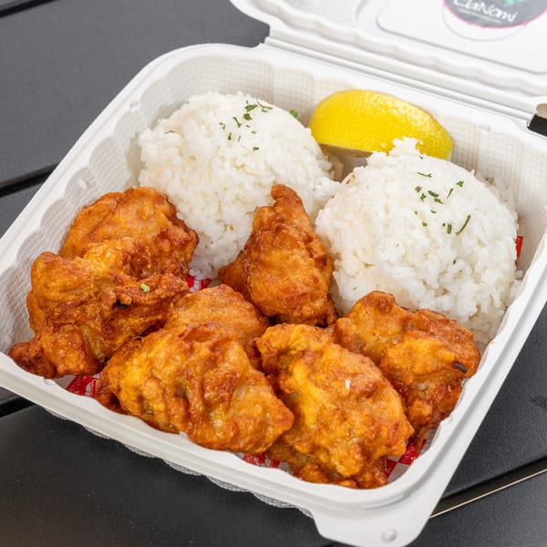 A takeout container filled with golden-brown fried chicken, white rice, and a lemon wedge.