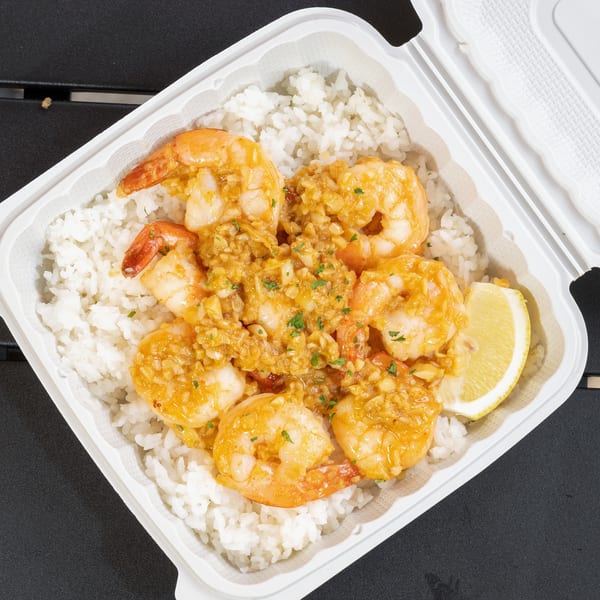 Garlic shrimp with white rice and a lemon wedge in a white takeout container from EbiNomi.