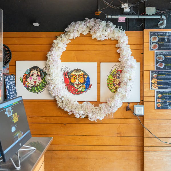 A wooden wall with three colorful Japanese-style paintings, framed by a white floral wreath.