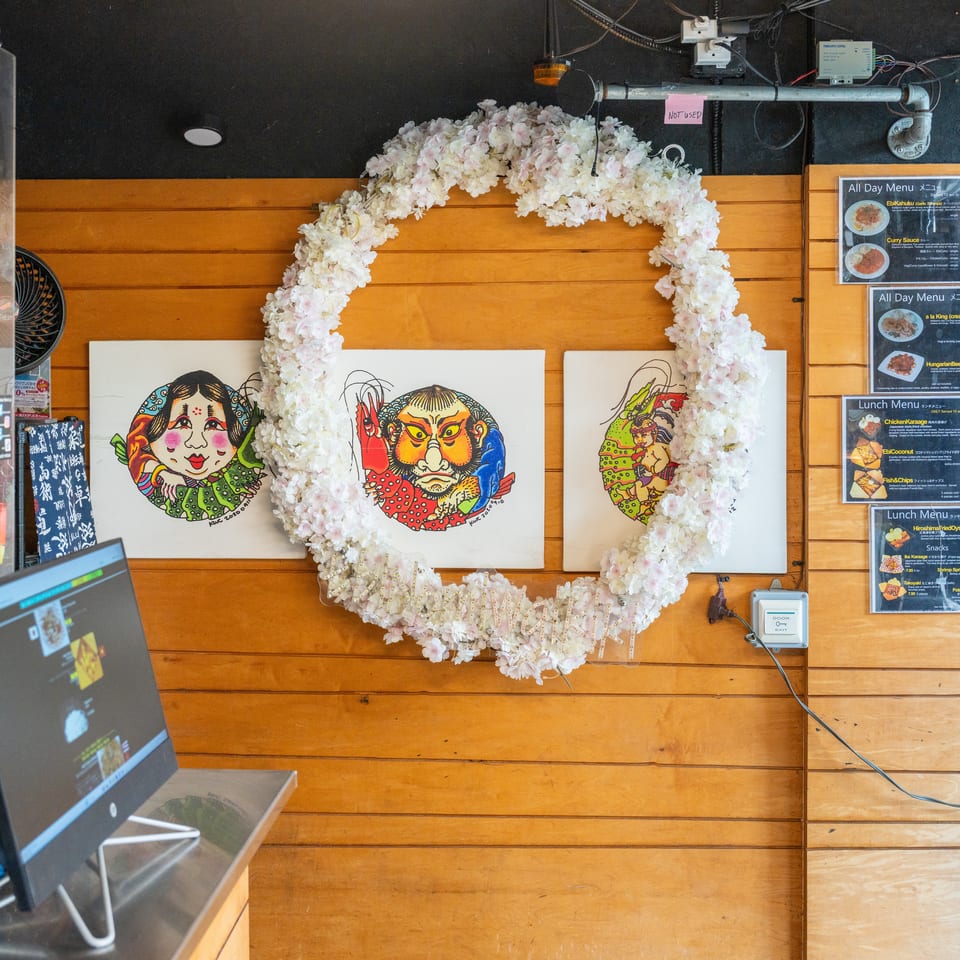 A wooden wall with three colorful Japanese-style paintings, framed by a white floral wreath.