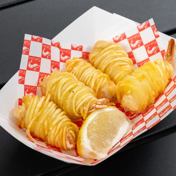 Five crispy potato-wrapped shrimp with a lemon wedge in a checkered paper tray.