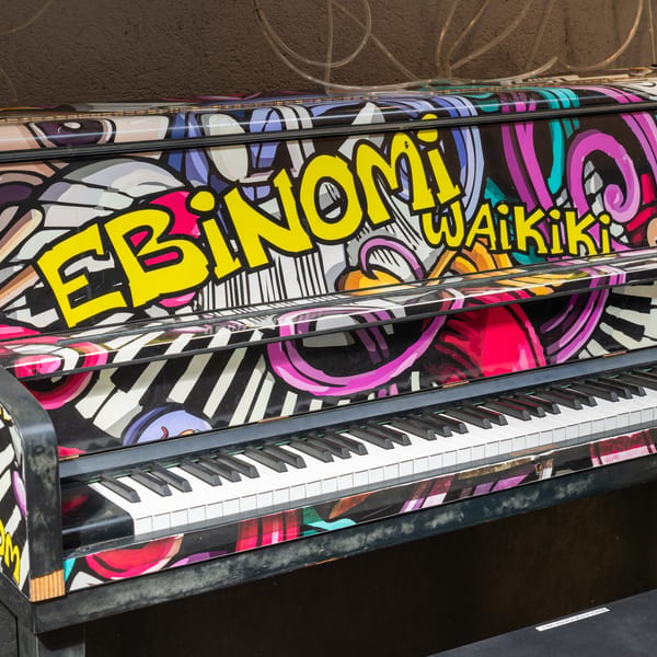 An upright piano with colorful graffiti art, featuring "EBINOMI Waikiki" in yellow letters.