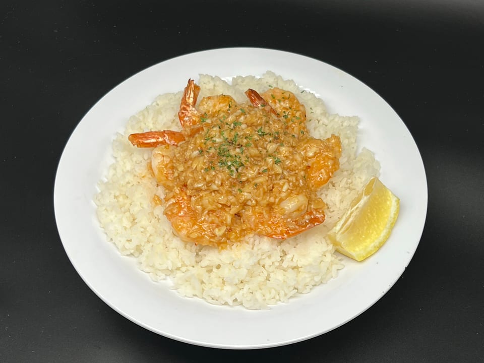 Garlic shrimp with rice and a lemon wedge on a white plate against a dark background.