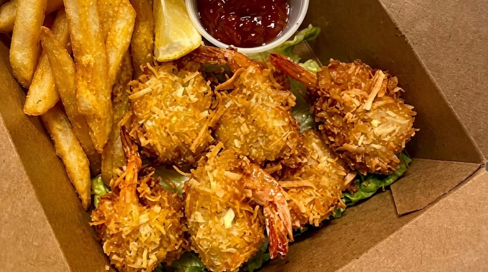 Crispy coconut shrimp, golden french fries, a lemon wedge, and dipping sauce in a takeout container.