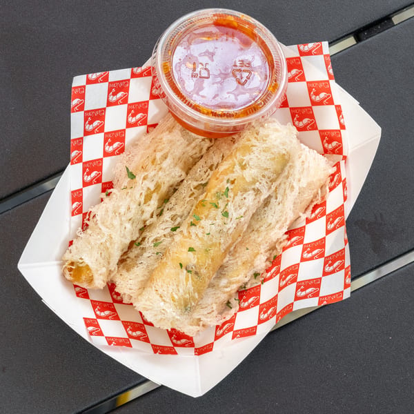 Three crispy shrimp tempura rolls with sweet chili dipping sauce in a paper tray.