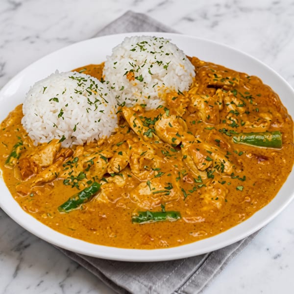 Chicken curry with green beans and two scoops of white rice, garnished with parsley.