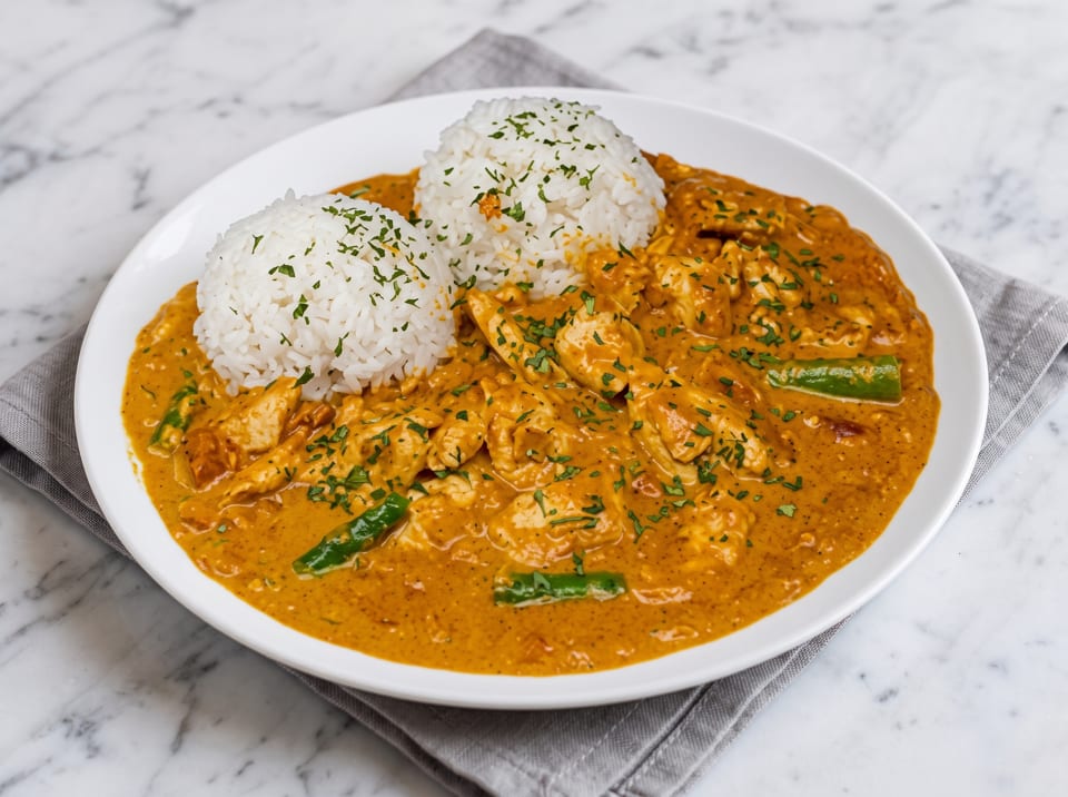 Chicken curry with green beans and two scoops of white rice, garnished with parsley.