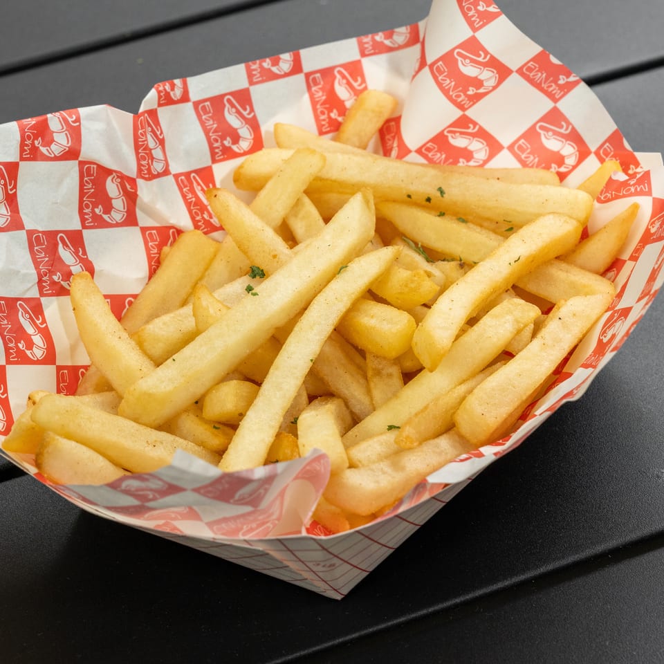 Golden french fries in a red and white checkered EbiNomi paper tray on a dark table.