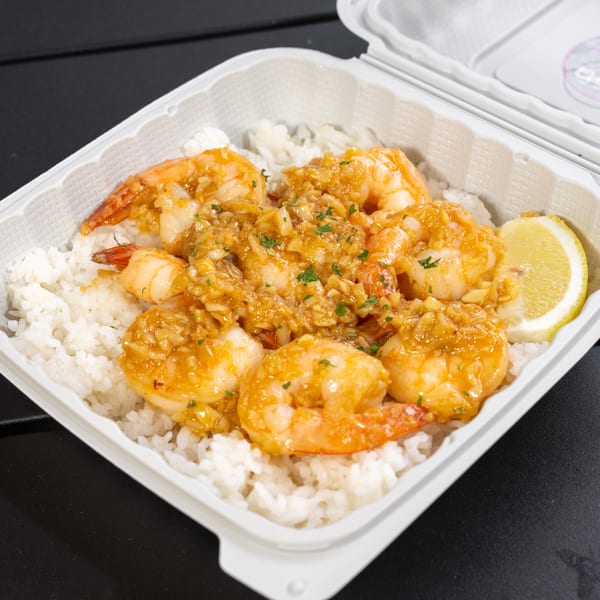 Garlic shrimp with white rice and a lemon wedge in a white takeout container.